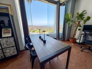 Ein stilvoller Essbereich mit einem Holztisch, Stühlen und Blick auf eine Landschaft durch große Fenster.