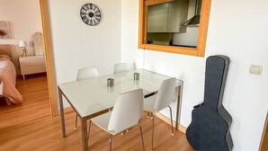Et spiseområde med et glastæppe og stole, et ur på væggen og en guitar kasse lænet mod væggen.