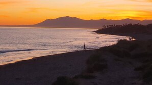 Paisaje costero con playa, océano y montañas distantes al atardecer.