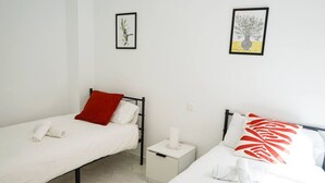 Una habitación con dos camas individuales, cada una con una almohada y una toalla enrollada. Hay cuadros en la pared.
