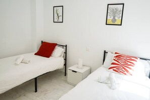 Ein Zimmer mit zwei Einzelbetten, jeweils mit Kissen und zusammengelegtem Handtuch. An der Wand befinden sich Bilder in Rahmen.