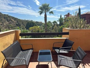 A balcony with four chairs and a small table, overlooking a hilly landscape with trees and buildings. - Relaxing 2 Bed duplex: seaviews, terrace & rooftop (Marbella)