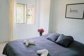 Een slaapkamer met een bed, kussens, een raam en een bord aan de muur.