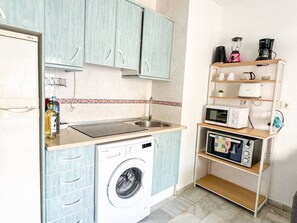 A compact kitchen with a washing machine, microwave, and a coffee maker on a shelf. - Torremolinos: Quiet 1bedroom with pool & sea views (Torremolinos)