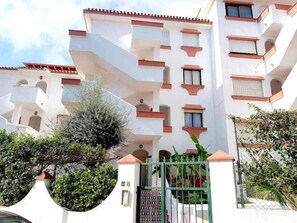 Un edificio residencial de varios pisos con balcones y una entrada protegida por una reja.