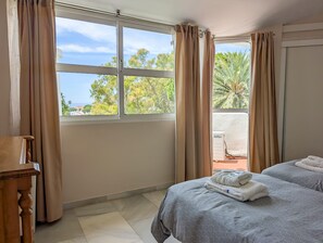 A hotel room with two beds, a wooden nightstand, and a window with curtains. - Pinos: Serene 2BD w/pool, views & walk to beach (Mijas)