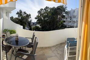 A patio with a round table and chairs, a small decorative item, and a view of a residential area with trees and buildings. - Pinos: Serene 2BD w/pool, views & walk to beach (Mijas)