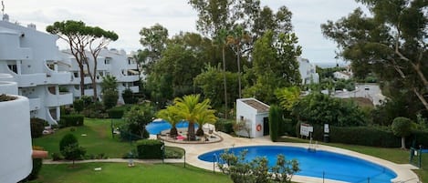 A residential area with a swimming pool, white buildings, and green lawns.