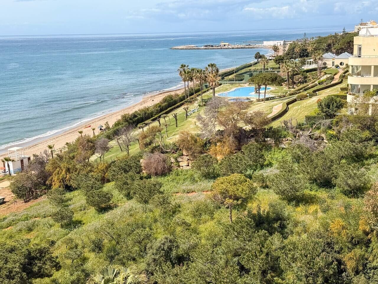 A coastal property with a beach, pool, and landscaped garden.