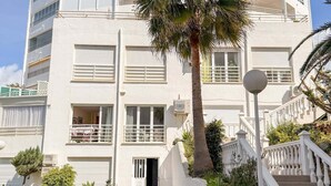 Un immeuble à plusieurs étages, doté de balcons, d’un palmier et d’un escalier menant à l’entrée.