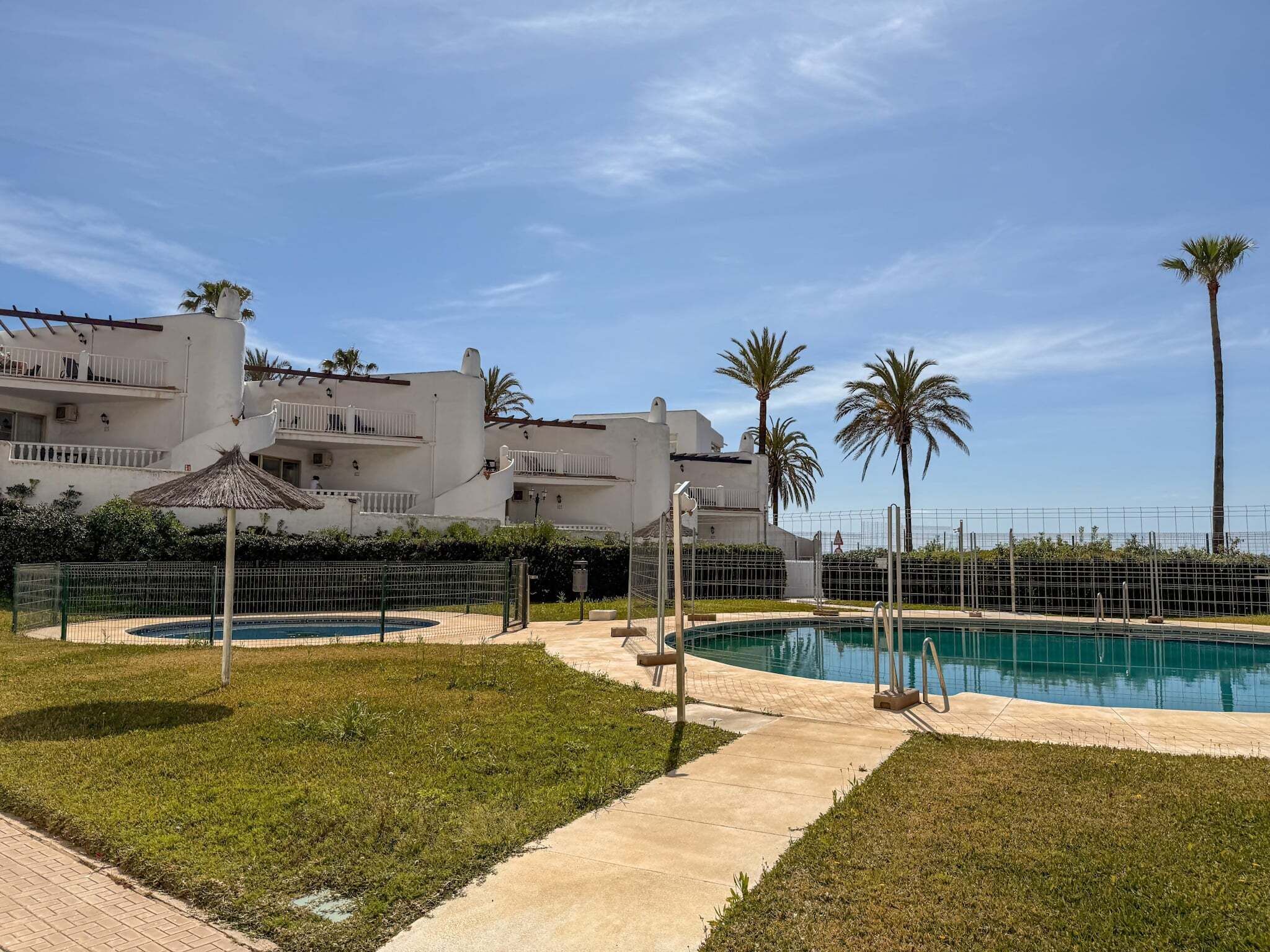 Una piscina con valla perimetral, césped y un edificio con balcones.
