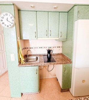 A kitchen with green cabinets, a sink, a coffee maker, and a clock. - Casa La Luna: ¡Cozy and sunny 1BR on the beach! (Mijas)