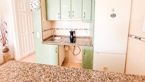 Une cuisine avec des meubles de couleur verte, un réfrigérateur blanc et une horloge au mur.