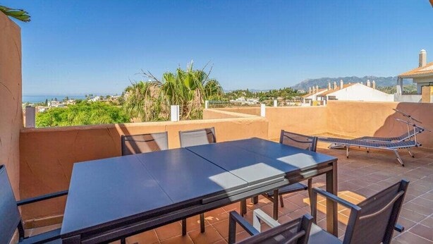 Une terrasse avec une table et des chaises, un hamac et une vue sur la mer et les montagnes.