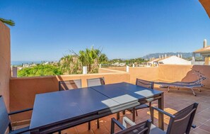Una terraza con mesa y sillas, una hamaca y vistas al mar y las montañas.