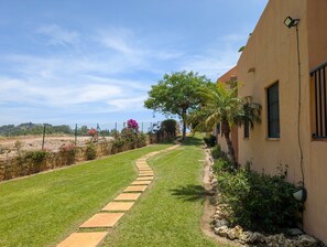 A pathway leading to a building with a stone border, surrounded by greenery and a fence. - Casa Lila: Sunny 2bed in Marbella (Marbella)