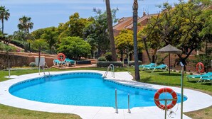 Une piscine à bordures courbes, entourée de pelouse et d’arbres, avec des chaises longues et une bouée de sauvetage visibles.
