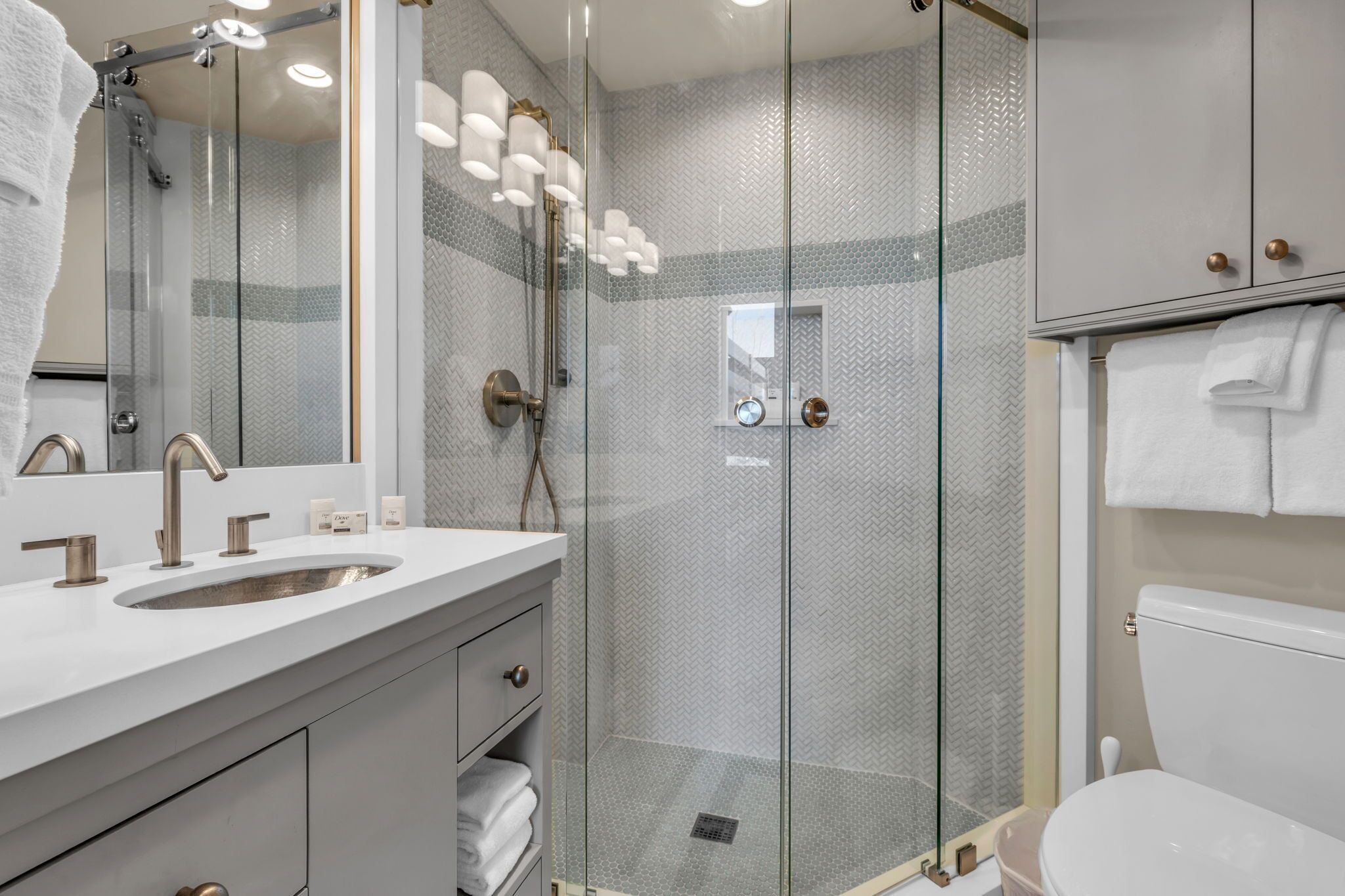 A modern bathroom with a glass-enclosed shower, a large mirror, and a white sink with two faucets.