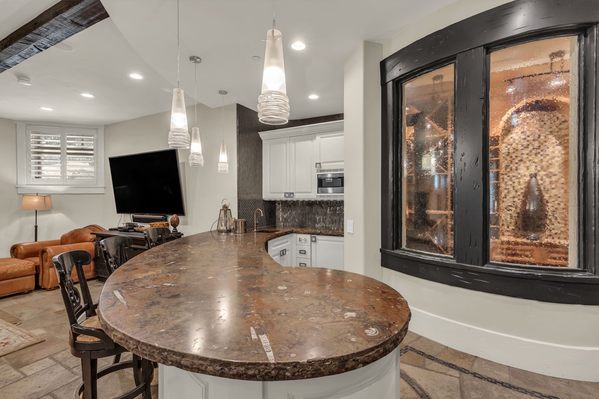 A modern kitchen with a curved island, pendant lighting, and a large window with a view.