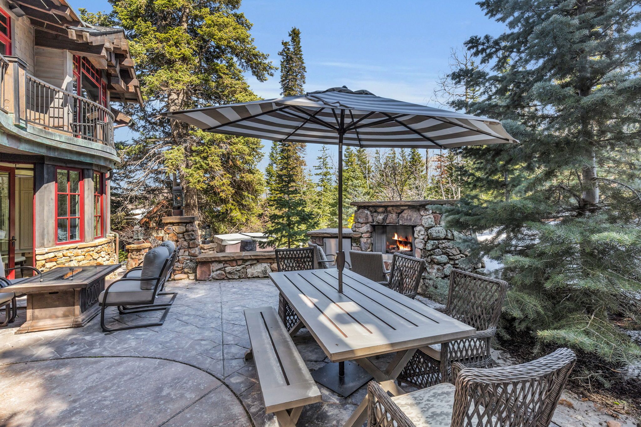 An outdoor patio with a stone fireplace, wooden table, and chairs.