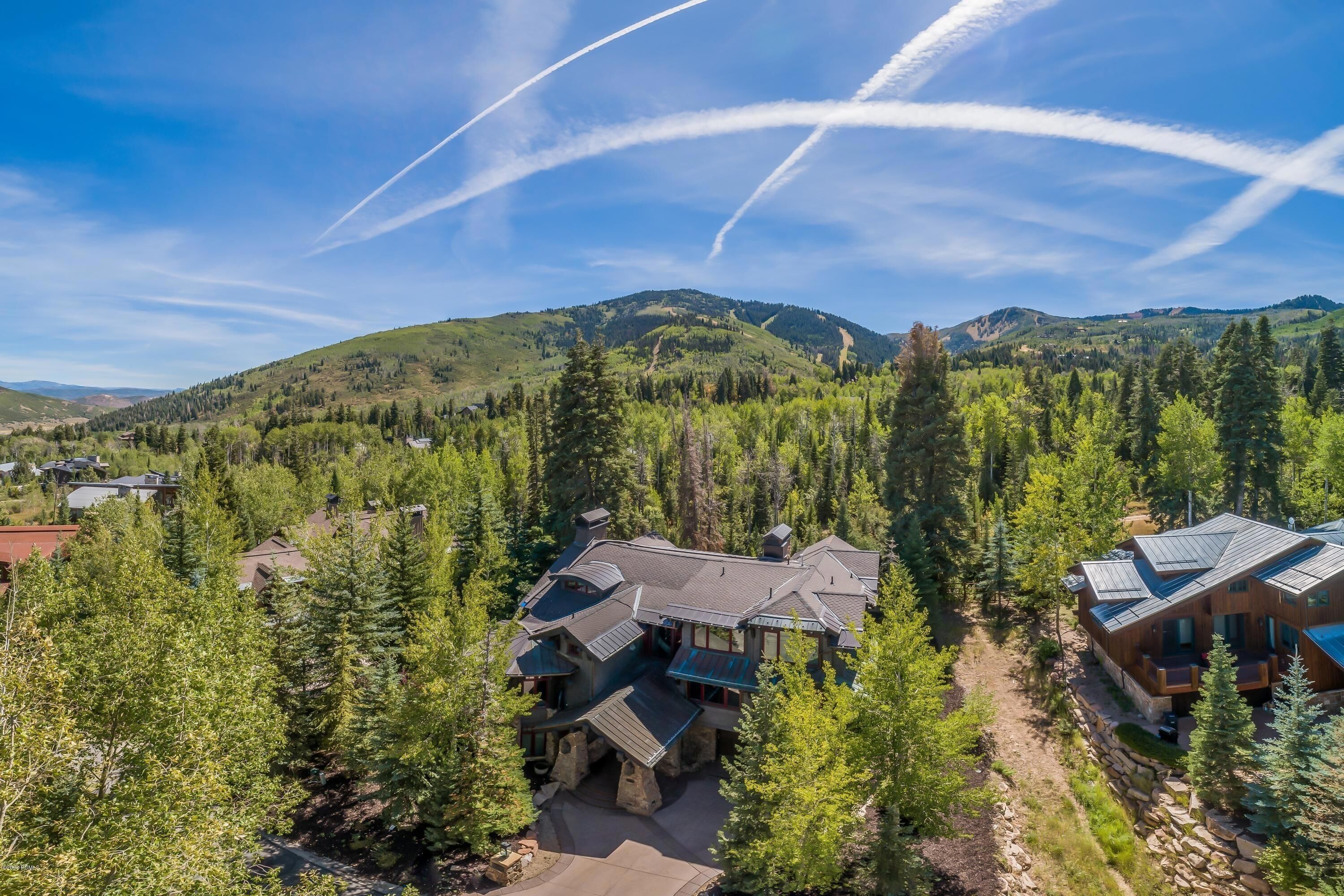 A lodge with a stone facade, surrounded by dense forest and mountains.