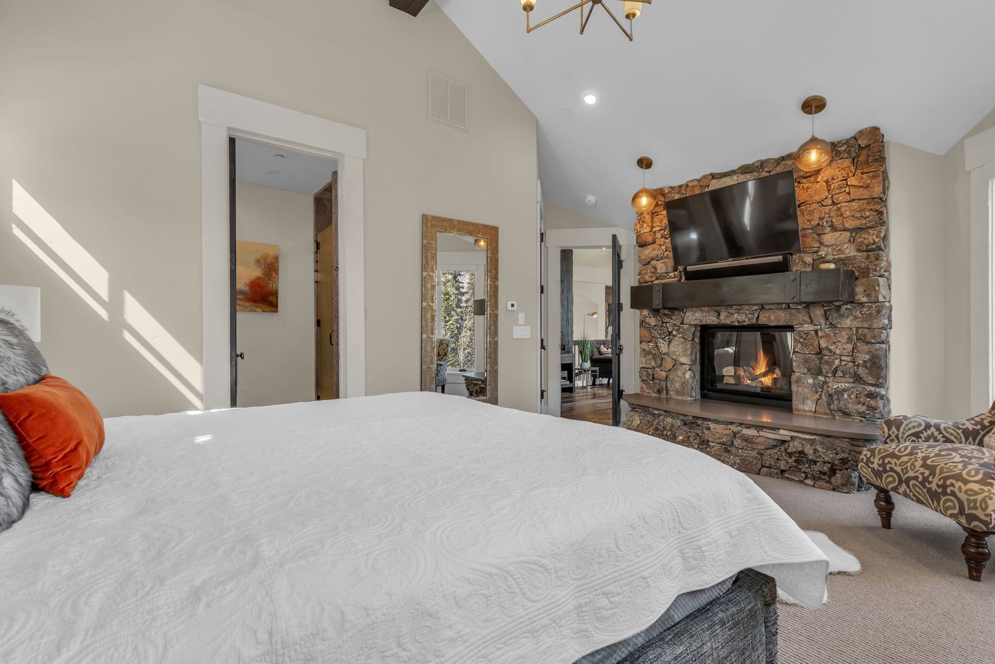 A bedroom with a large bed, a stone fireplace, and a television mounted on the wall.