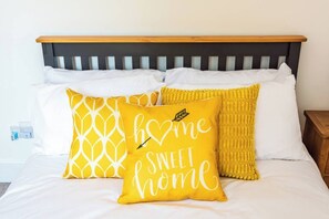 A bed with a wooden headboard, white bedding, and three pillows with yellow and white patterns.
