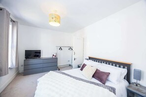 A bedroom with a bed, a dresser, a TV, a wardrobe, and a hanging coat rack.