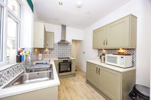 A kitchen with a sink, stove, oven, microwave, and cabinets. - Spacious 3BR House Near Sixfields, Duston (Northampton)