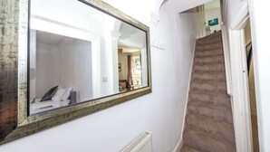 Een hal met een grote spiegel, een radiator en een trap.