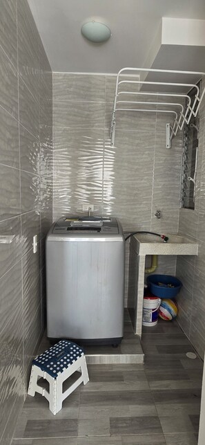 A compact bathroom with a washing machine, a small stool, a sink, and a blue basin. - Beautiful vacation apartment (Girardot)
