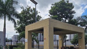 Ein kleines, offenes Pavillon mit Betondach und -wänden, umgeben von einem gepflegten Garten mit roten Blumen.