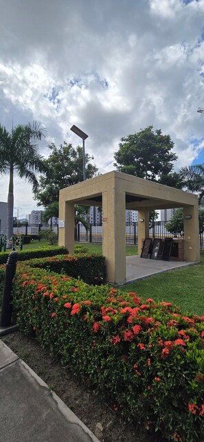 A small, open-air pavilion with a concrete roof and walls, surrounded by a well-maintained garden with red flowers. - Beautiful vacation apartment (Girardot)