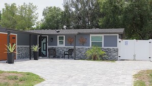 A modern house with a stone and wood exterior, a covered patio, and a fenced yard. - Sarasota Silver Oasis - Private Pool, Near Beaches & Downtown (Sarasota)