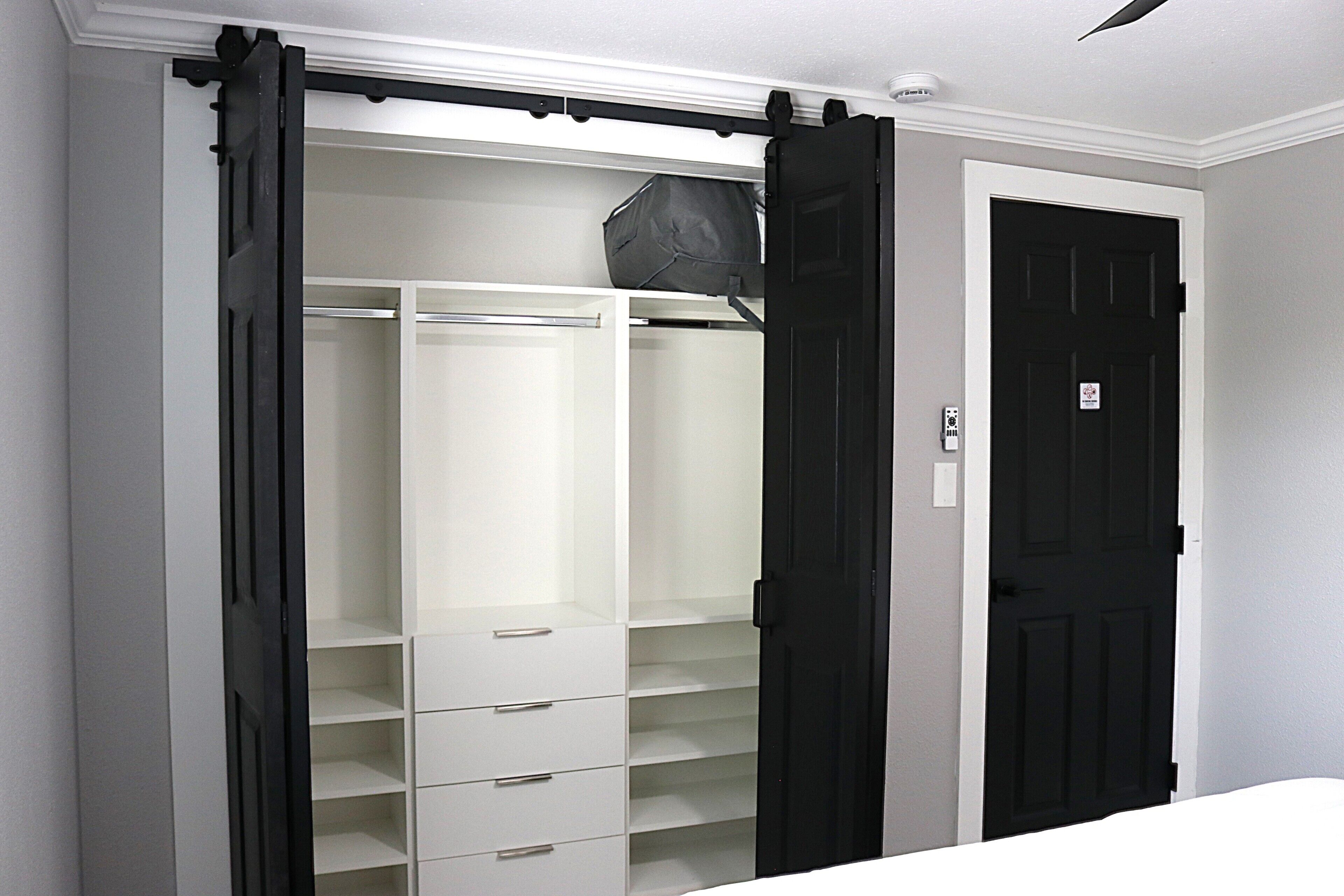 A walk-in closet with open doors, a black door, and a white wall.