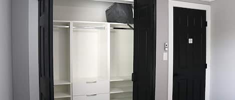 A walk-in closet with open doors, a black door, and a white wall.