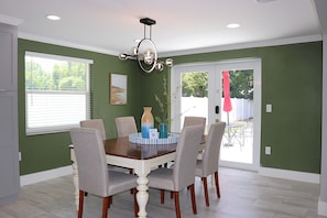 A dining room with a wooden table, six chairs, a chandelier, and a view of the backyard through a sliding glass door. - Sarasota Silver Oasis - Private Pool, Near Beaches & Downtown (Sarasota)