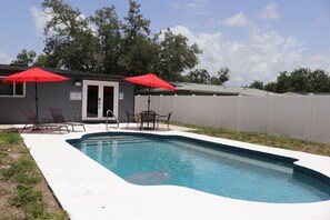 A swimming pool with two red umbrellas, a covered seating area, and a white fence. - Sarasota Silver Oasis - Private Pool, Near Beaches & Downtown (Sarasota)
