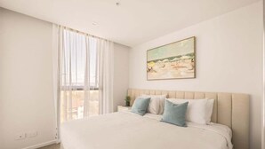 Ein Hotelzimmer mit einem großen Bett, einem Bild an der Wand und einem Fenster mit durchsichtigen Vorhängen.