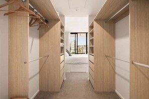 Un dressing accessible sans porte, avec des portes en bois, un lit et une vue sur les immeubles par une fenêtre.
