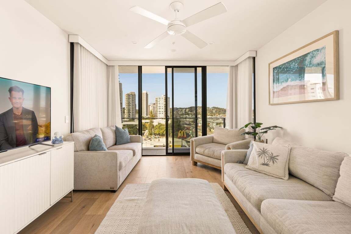 A modern living room with a flat-screen TV, two sofas, a coffee table, and a ceiling fan.