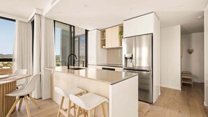Eine moderne Küche mit Kochinsel, Barhocker und einem Edelstahl-Kühlschrank.