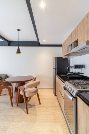 A modern kitchen with a gas stove, wooden cabinets, and a dining area with a round table and chairs. - Casa myla - Roma Norte (Mexico City)