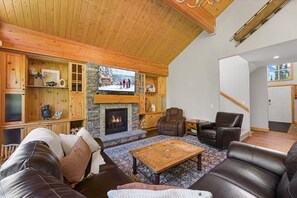 A cozy living room with a fireplace, leather sofas, a coffee table, and wooden shelving. - True Ski-In/Out Luxury Chalet • Hot Tub • Sauna (Big White)