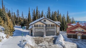 A two-story stone building with a ski lift access sign, surrounded by snow-covered trees and a clear sky. - True Ski-In/Out Luxury Chalet • Hot Tub • Sauna (Big White)