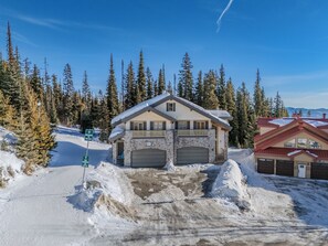 A two-story stone building with a ski lift access sign, surrounded by snow-covered trees and a clear sky. - True Ski-In/Out Luxury Chalet • Hot Tub • Sauna (Big White)