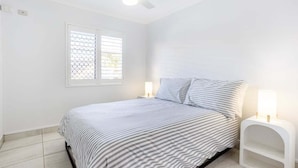 Ein Schlafzimmer mit einem Bett, einem Deckenventilator, einem Fenster mit Jalousien und Nachttischlampen.