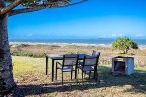 Ein Sitzbereich im Freien mit Tisch und Stühlen, ein Baum und Blick aufs Meer.