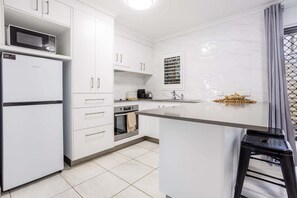 Eine moderne Küche mit weißen Schränken, einem eingebauten Backofen, einer Mikrowelle und einer kleinen Kücheninsel mit einem Hocker.