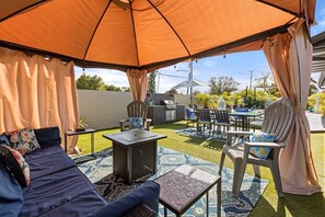 Eine Außenveranda mit einer Couch, Stühlen, einem Tisch und einem Sonnenschirm.